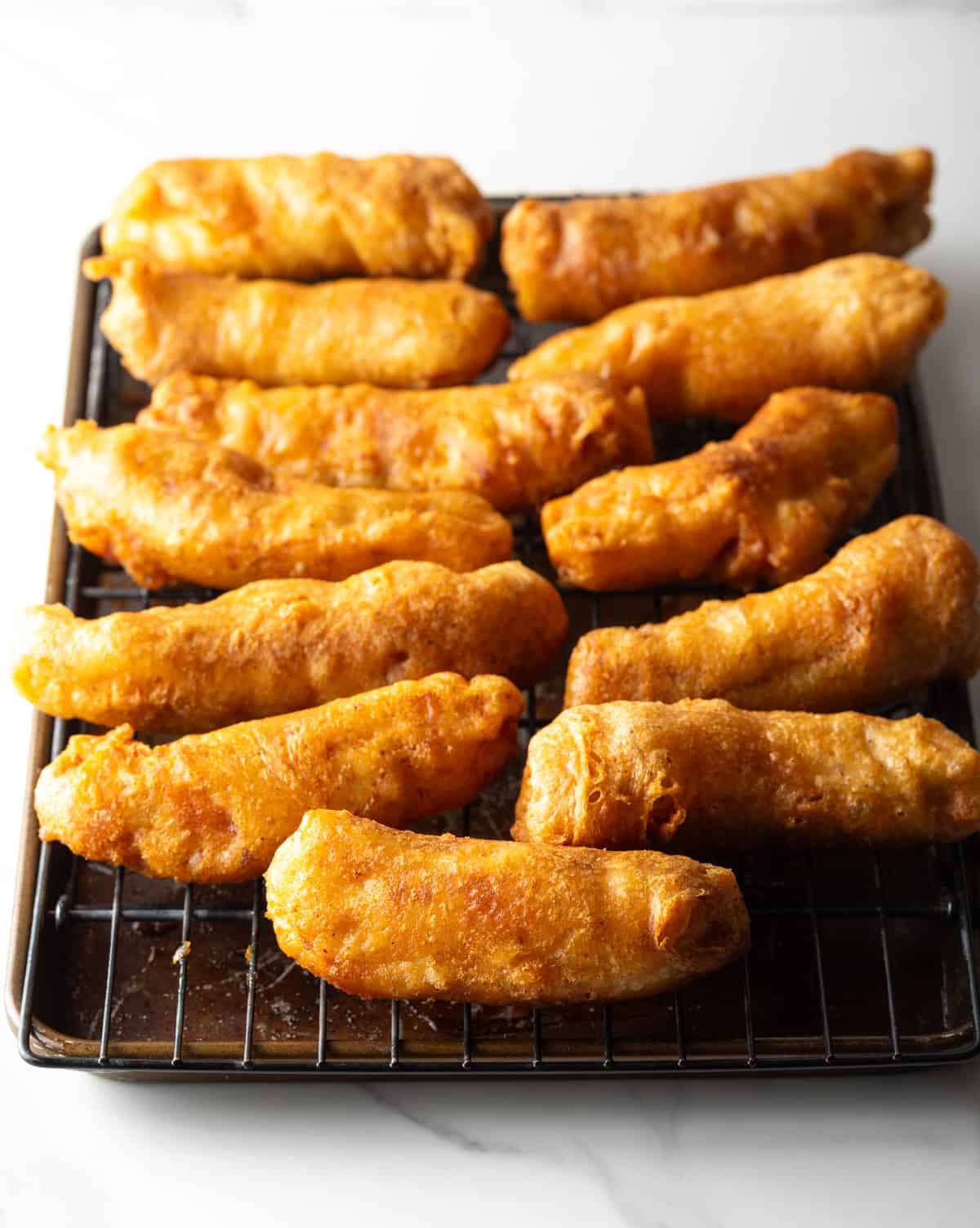 Crispy beer battered fish pieces lined up on a black drying rack.