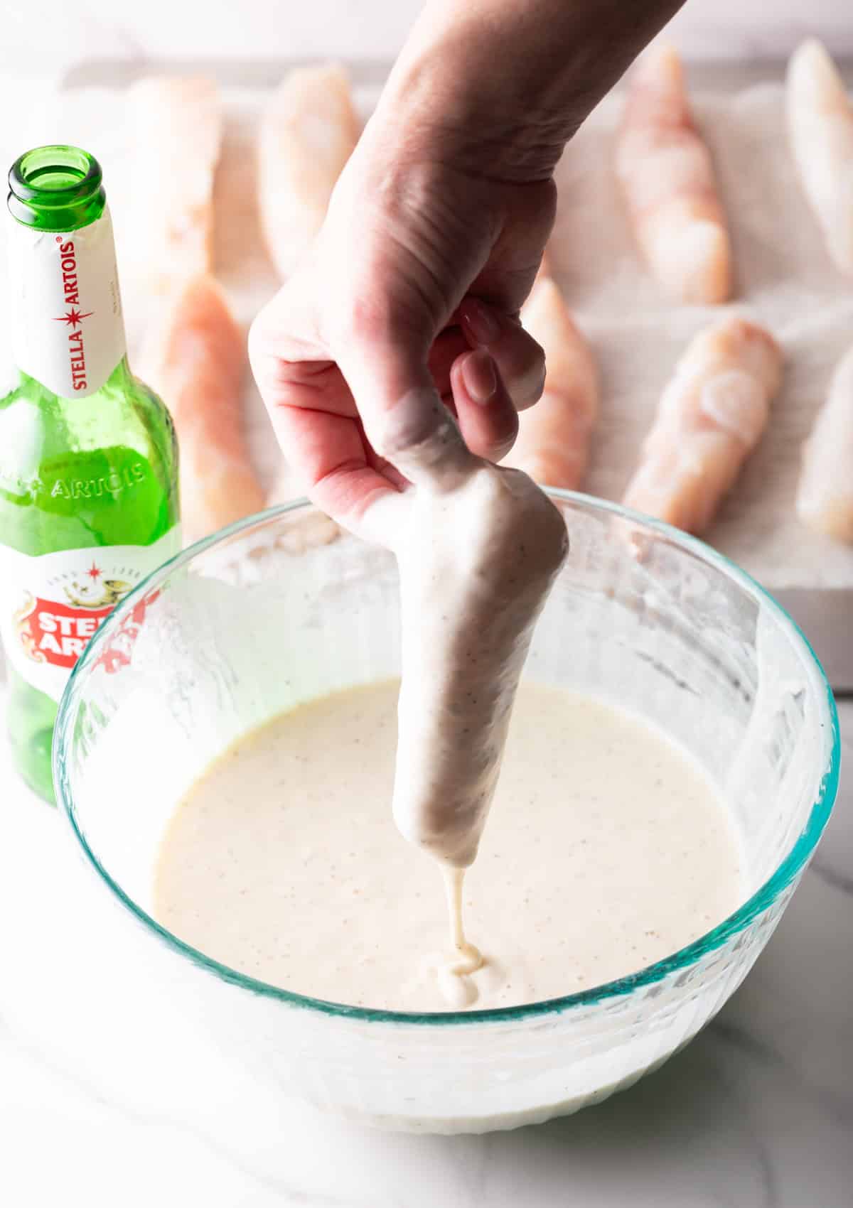 A hand is holding a fish fillet that is being dipped in a fish and chips batter.