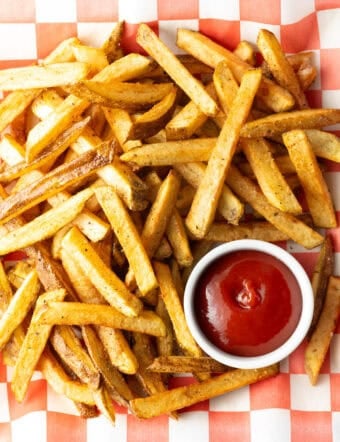 Top down view freshly fried potatoes in a pile with ramekin of ketchup on the side.