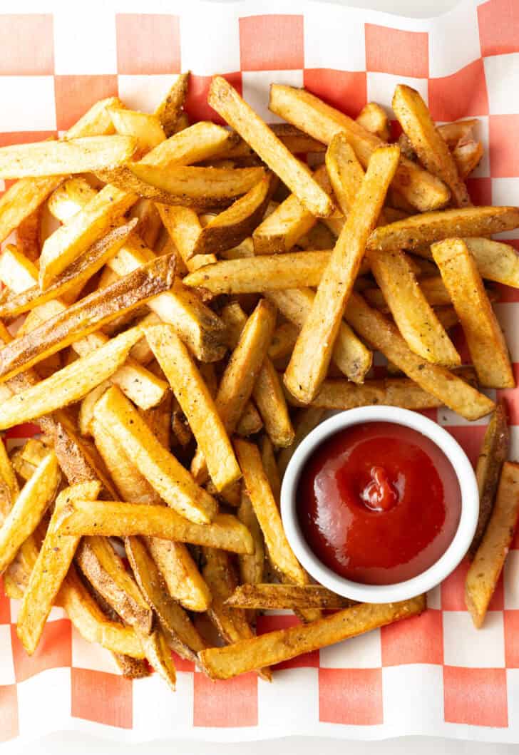 Top down view freshly fried potatoes in a pile with ramekin of ketchup on the side.
