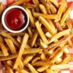 Top down view freshly fried potatoes in a pile with ramekin of ketchup on the side.