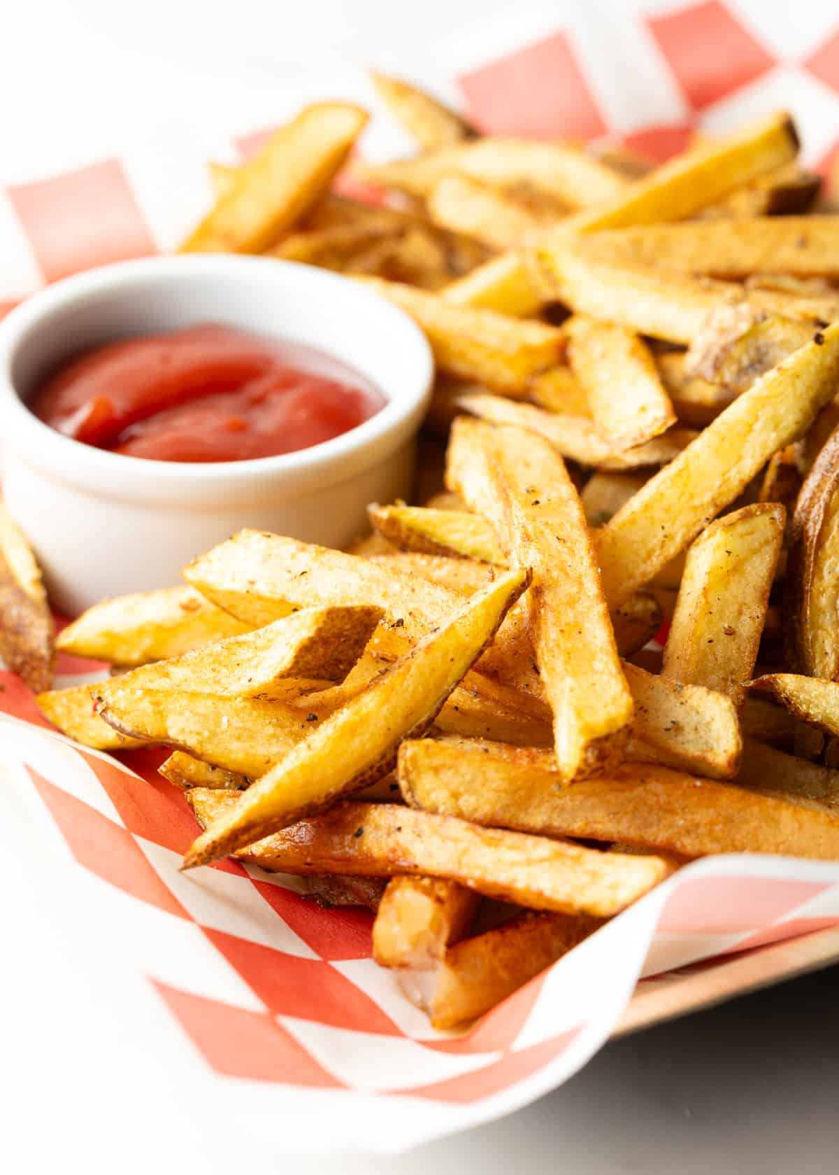 Red and white checkered basket loaded with homemade french fries and ramekin of ketchup.