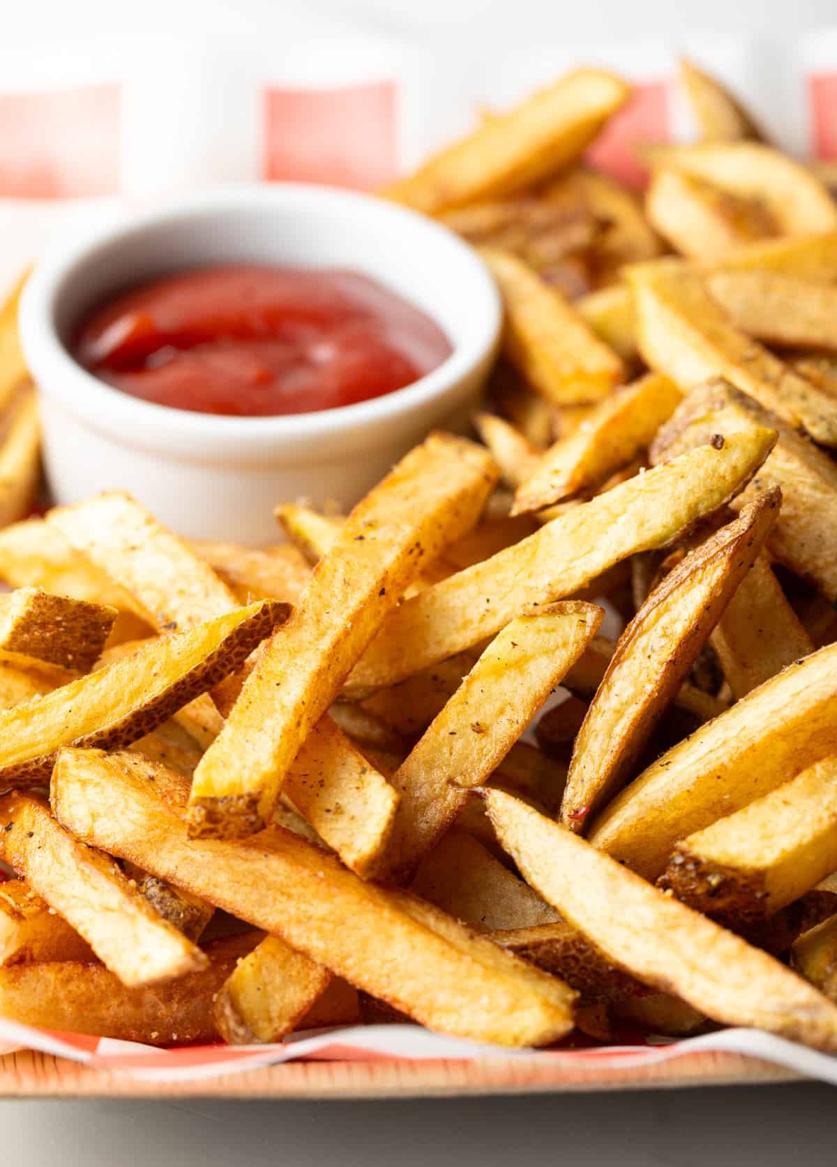 Red and white checkered basket loaded with homemade french fries and ramekin of ketchup.