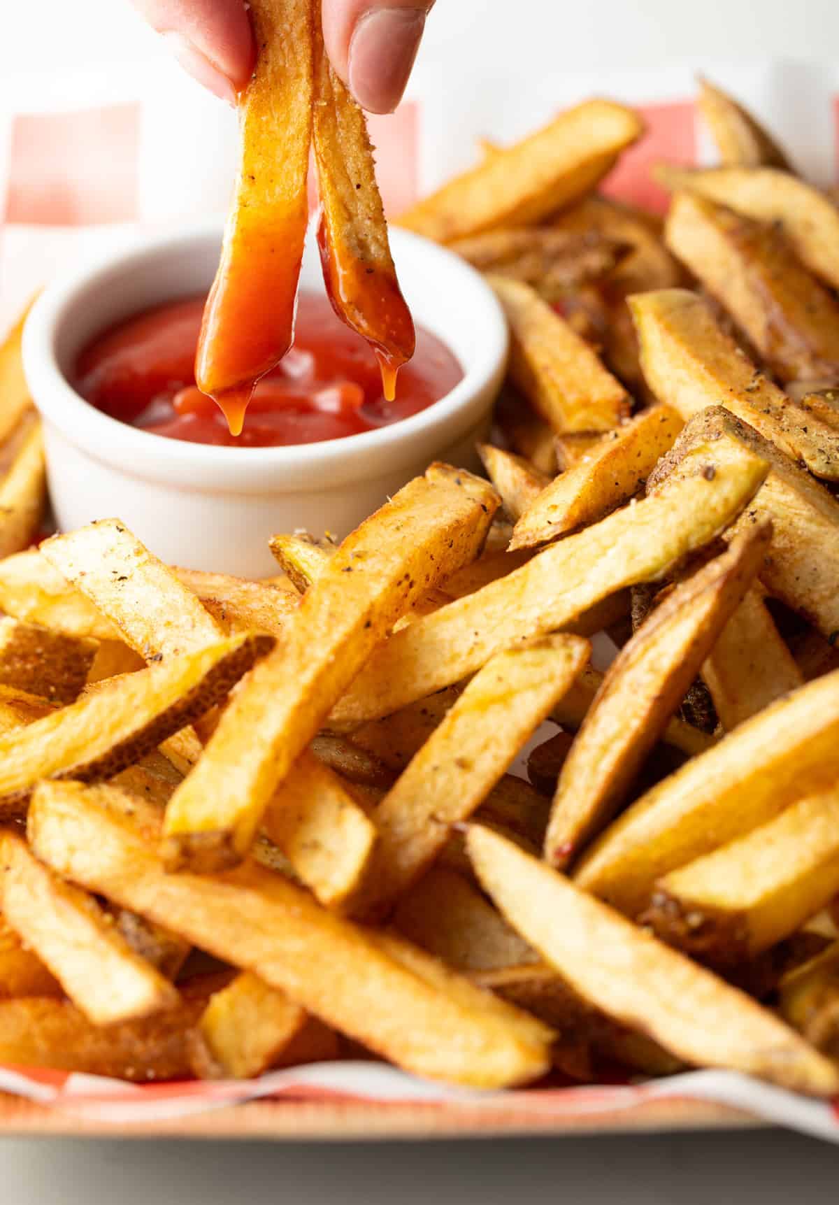 Hand dipping two homemade french fries into a ramekin of ketchup.