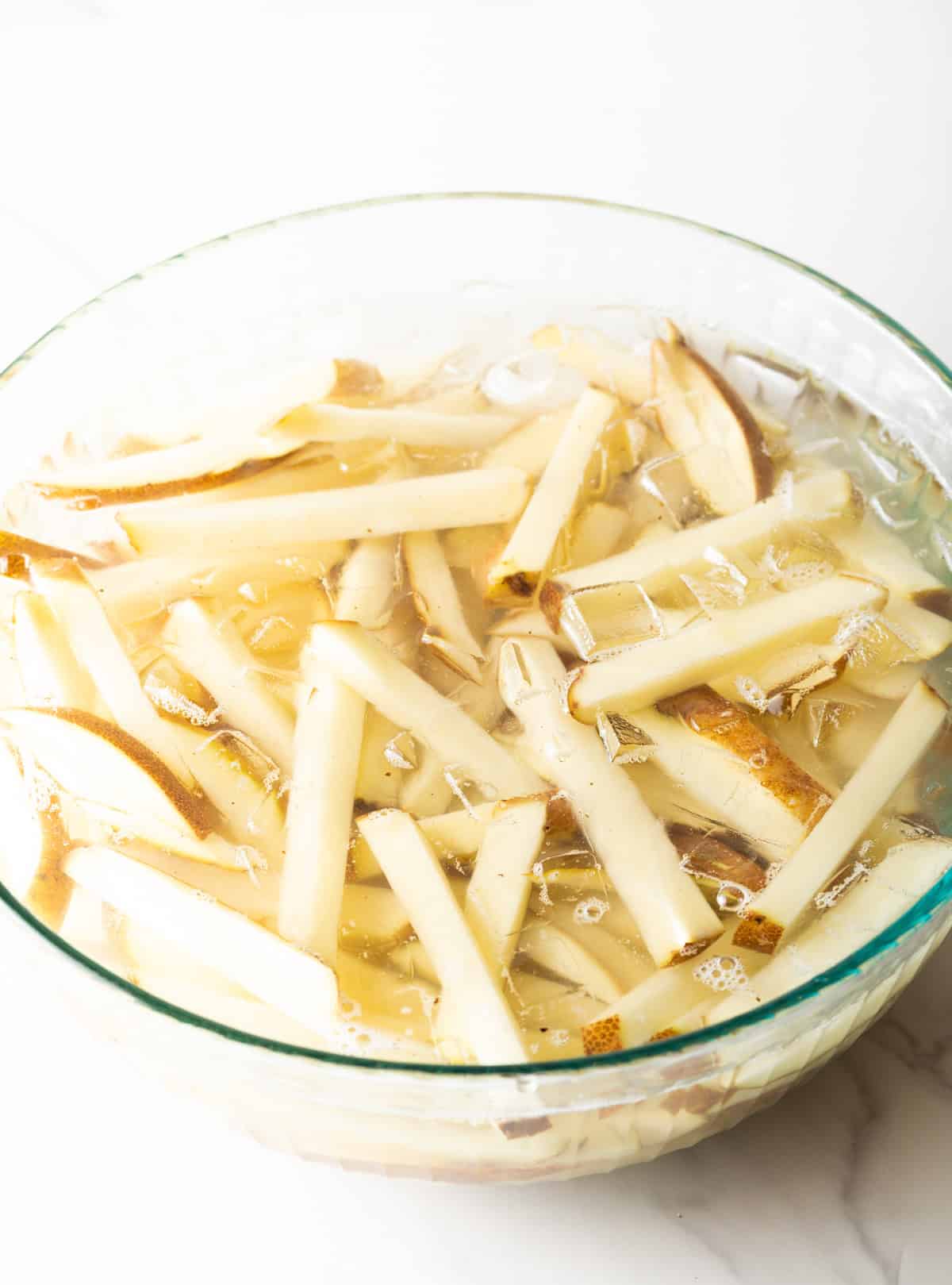 Slices of raw potato in a large glass bowl of water.