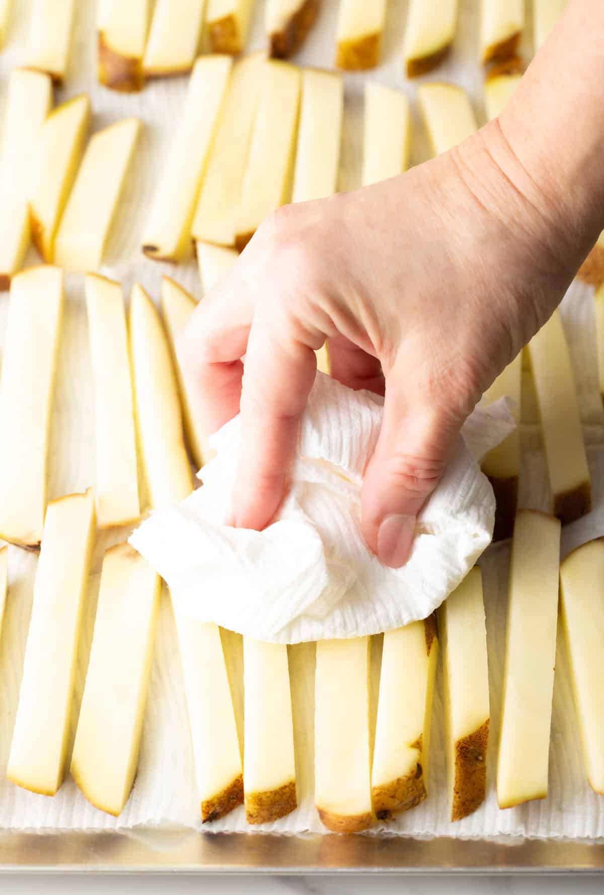 Hand blotting moisture from rows of raw sliced potatoes.