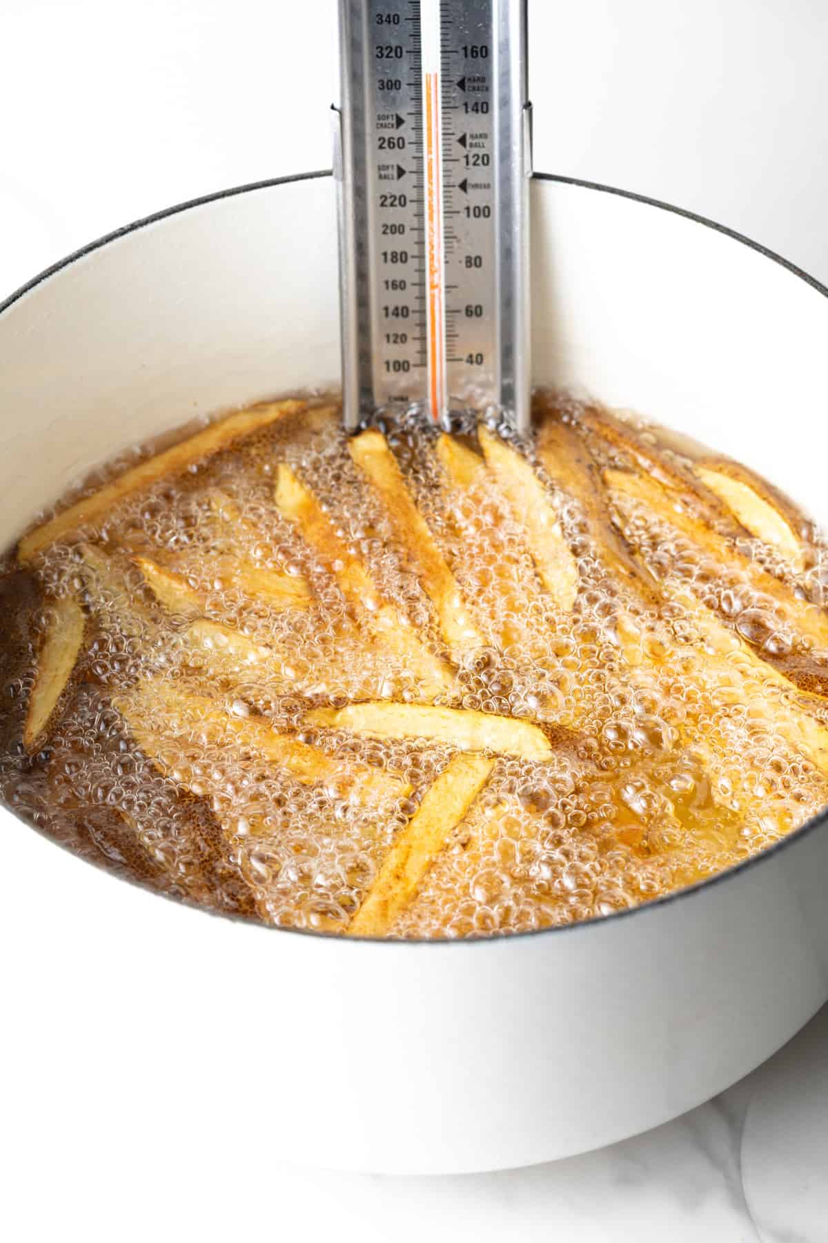 Boiling thick slices of potatoes in a white pot of oil, with a thermometer clipped on the side.
