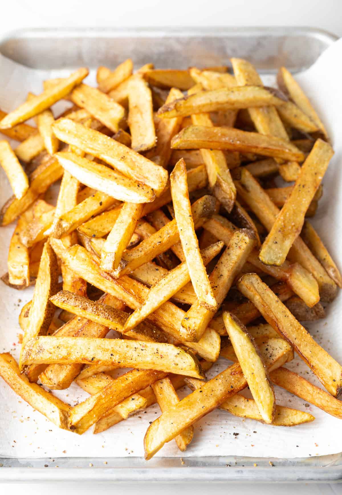 Top down view freshly fried potatoes in a pile on a baking sheet.