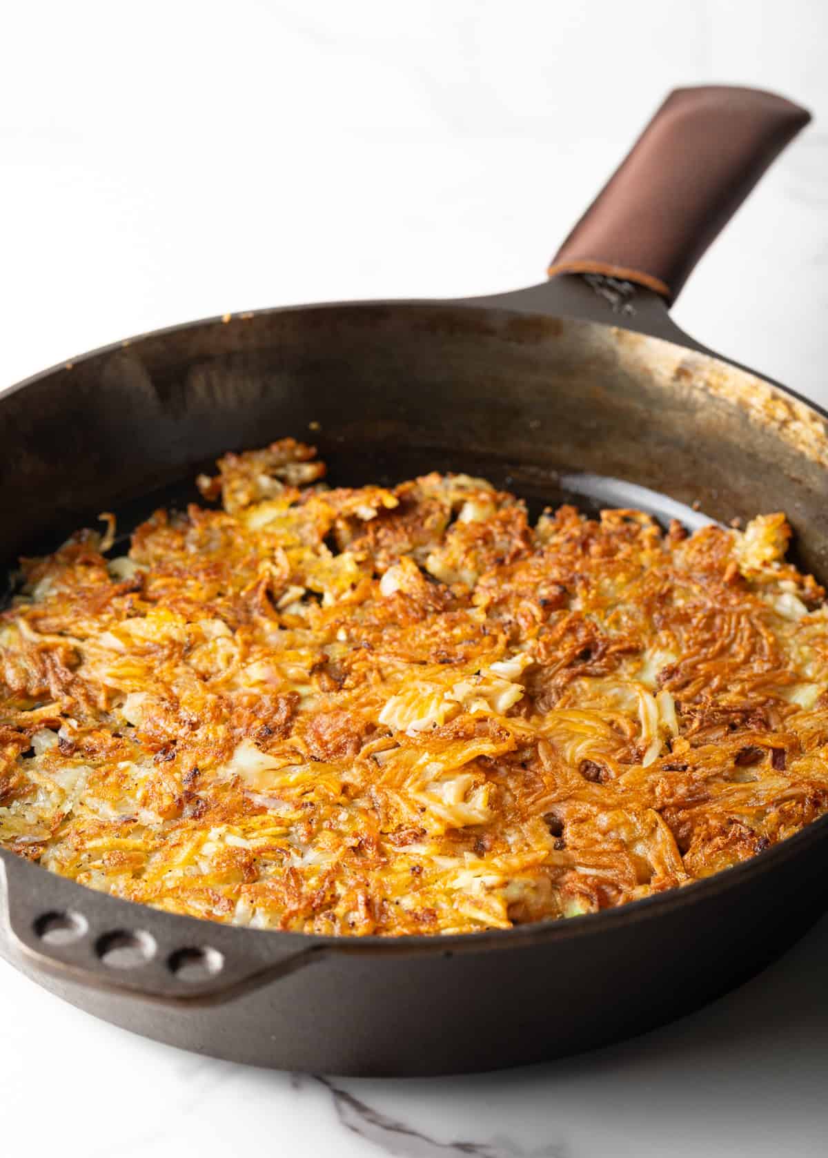Golden and crispy homemade hashbrowns in a black skillet.
