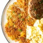 Crispy homemade hash browns, breakfast sausage, and scrambled eggs on a white plate.