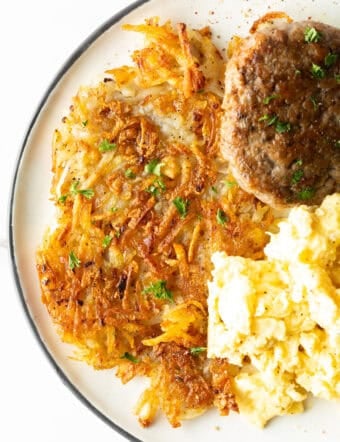 Crispy homemade hash browns, breakfast sausage, and scrambled eggs on a white plate.