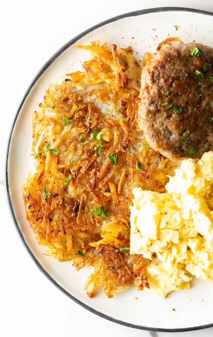 Crispy homemade hash browns, breakfast sausage, and scrambled eggs on a white plate.