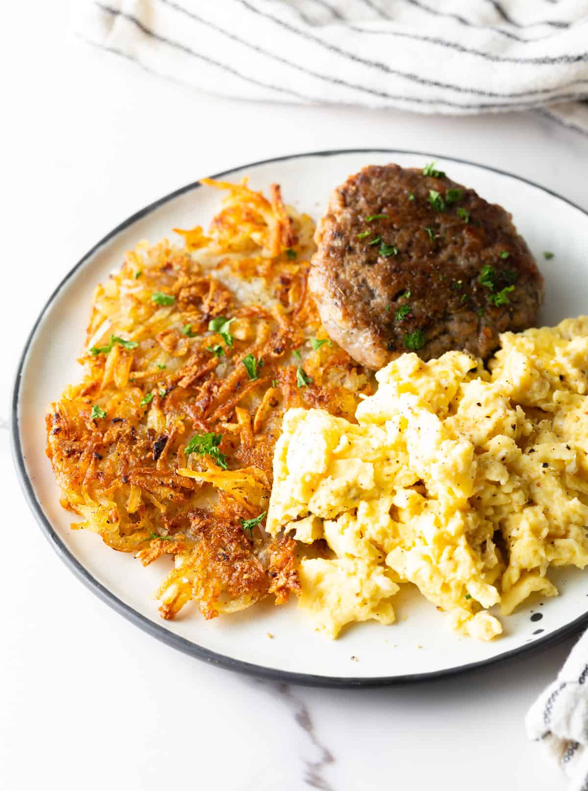 A white plate filled with homemade hash brown potatoes, breakfast sausage, and scrambled eggs.