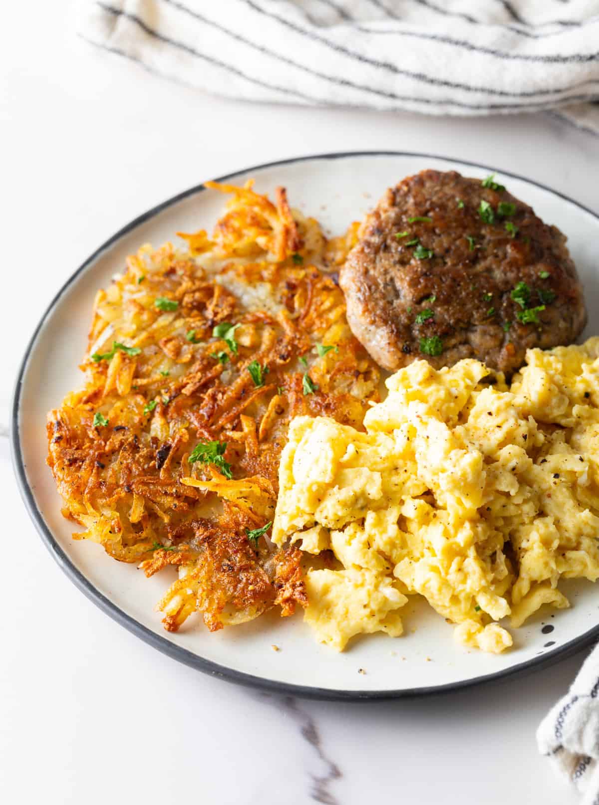 A white plate filled with homemade hash brown potatoes, breakfast sausage, and scrambled eggs. 