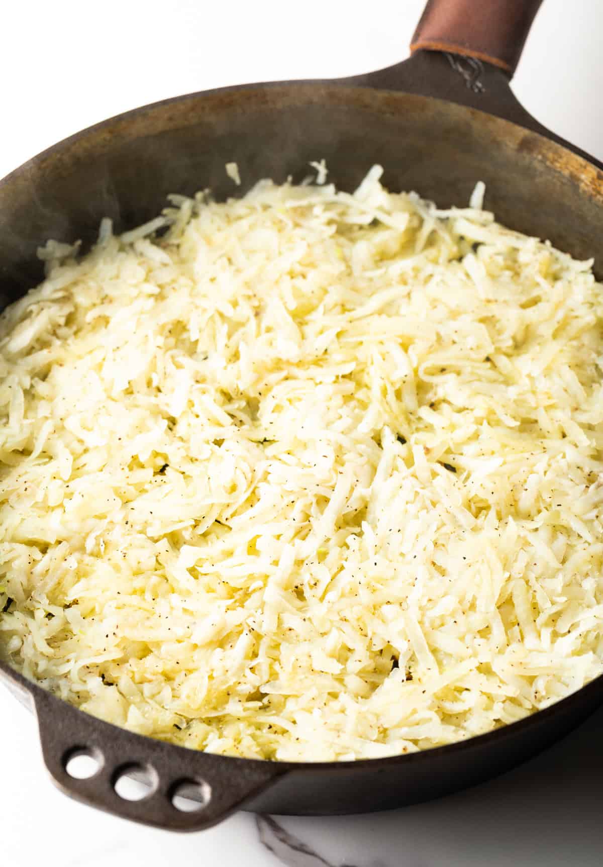 Overhead shot of raw shredded potatoes in a black skillet.