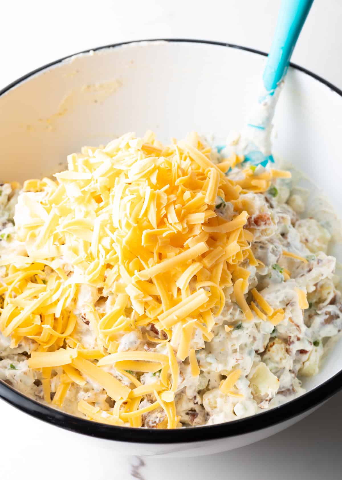 A bowl filled with loaded baked potato salad, topped with shredded cheddar cheese.