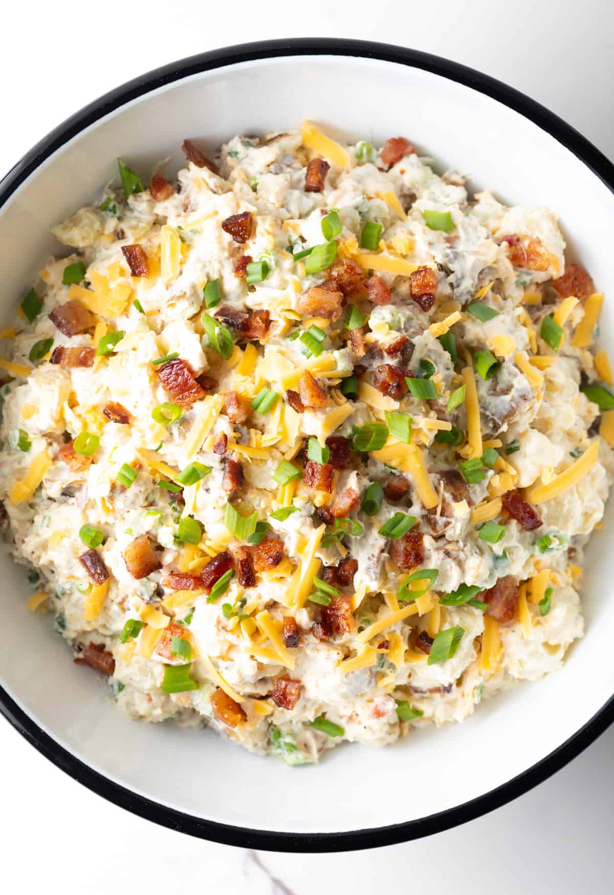 An overhead shot of a loaded baked potato salad recipe in a white bowl.