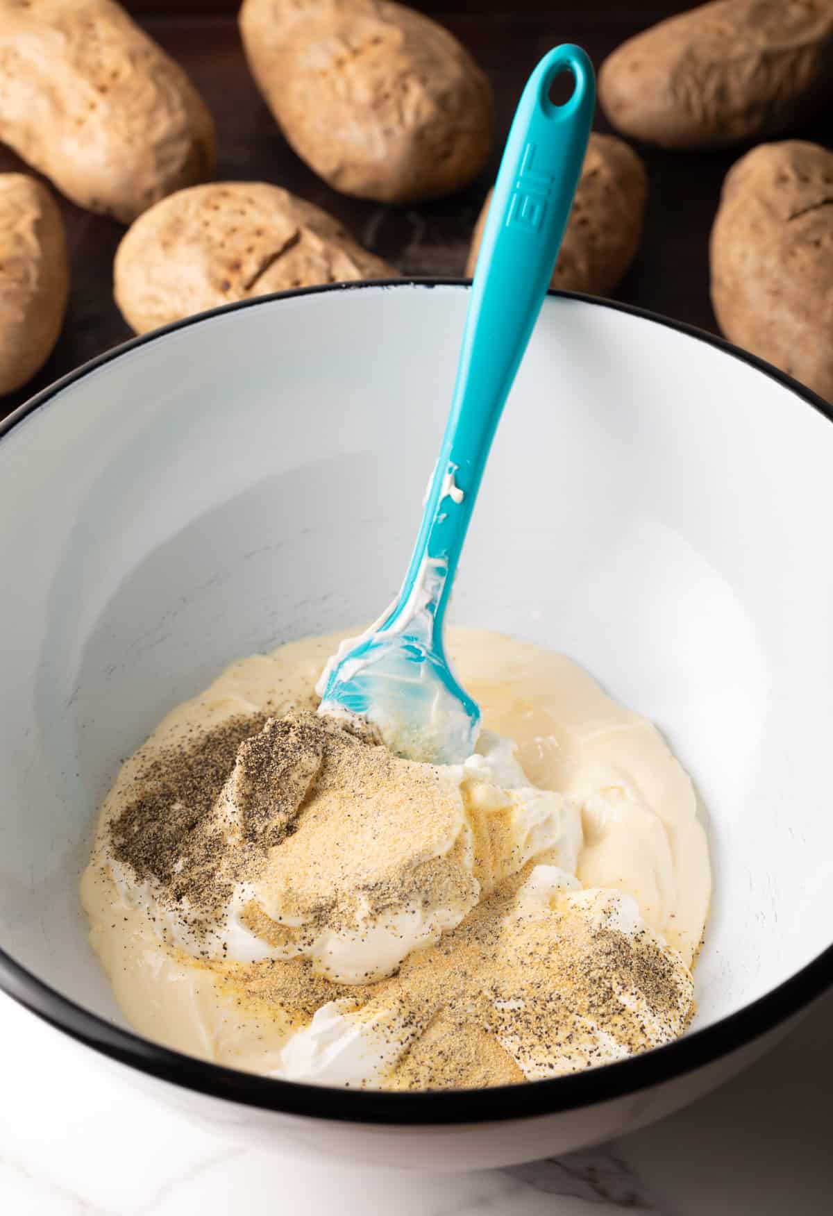 Ingredients for the dressing for a baked potato salad recipe are being stirred in a white bowl.