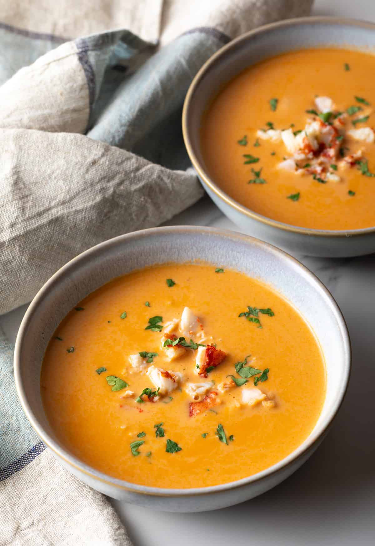 Two bowls of creamy lobster bisque soup topped with lobster chunks and parsley.
