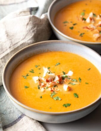 A bowl of creamy lobster bisque soup topped with lobster chunks and parsley.