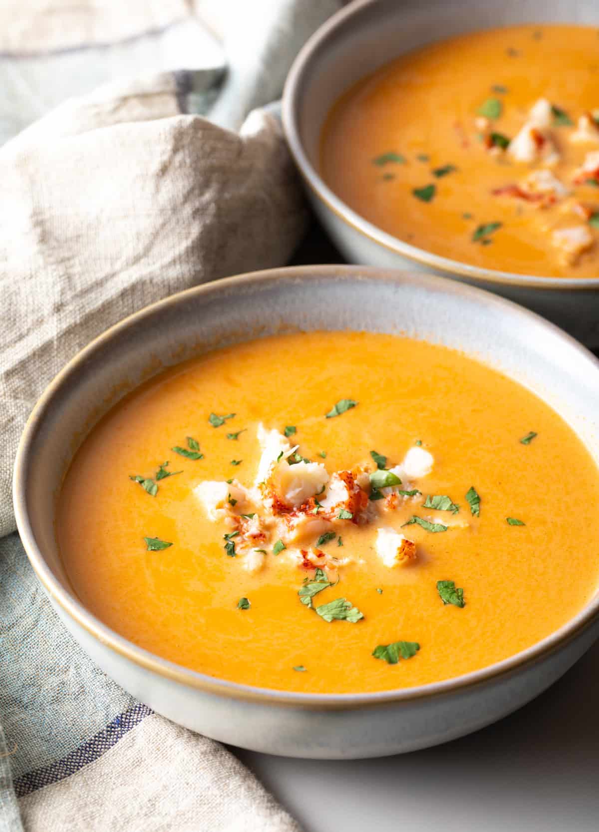 A bowl of creamy lobster bisque soup topped with lobster chunks and parsley.