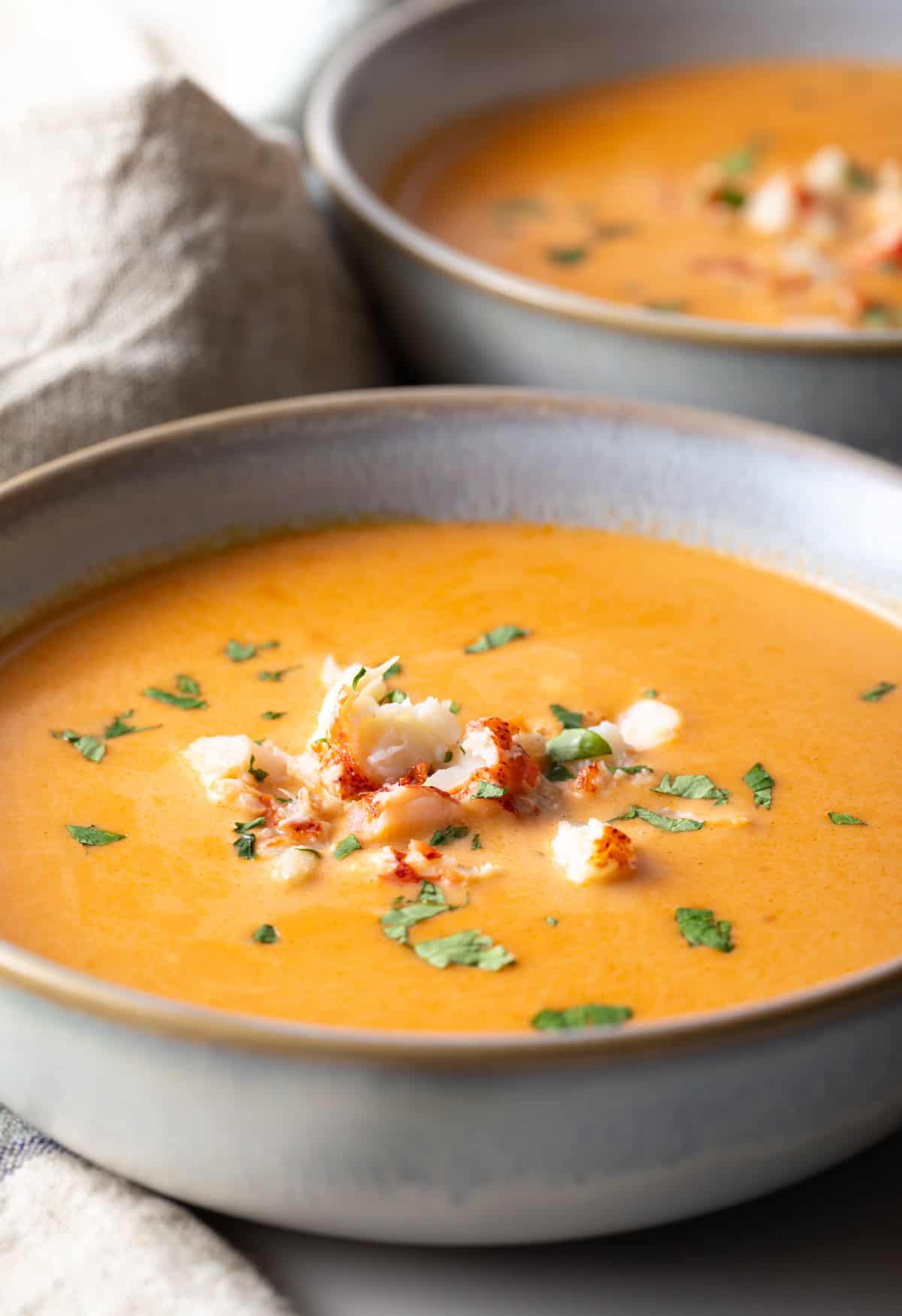 A bowl of creamy lobster bisque soup topped with lobster chunks and parsley.