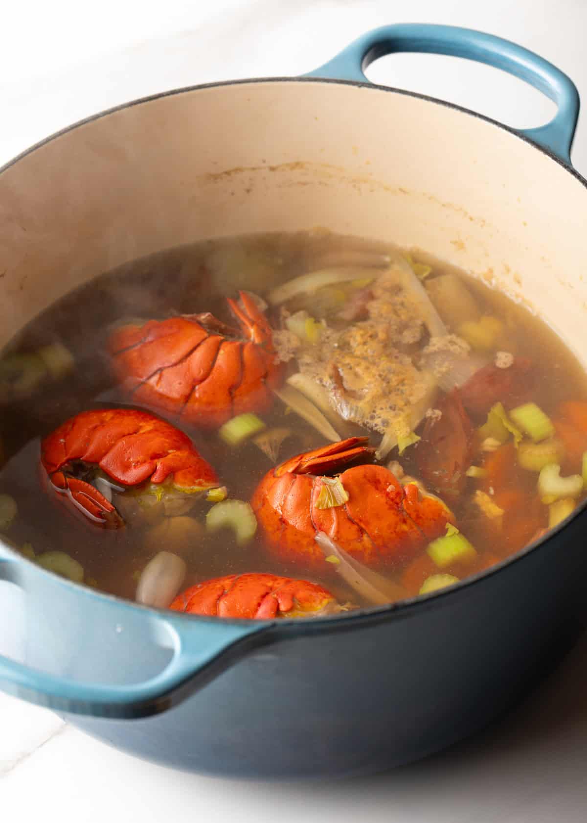 A pot simmering with seafood stock, lobster, and veggies.