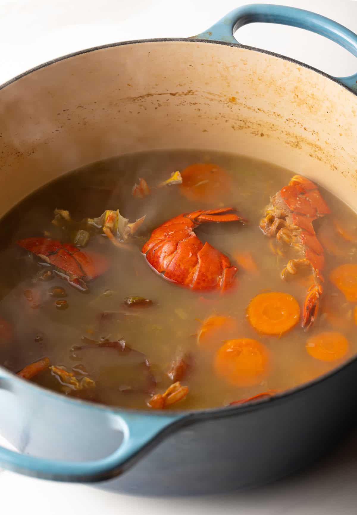A pot simmering with seafood stock, lobster shells, and veggies.