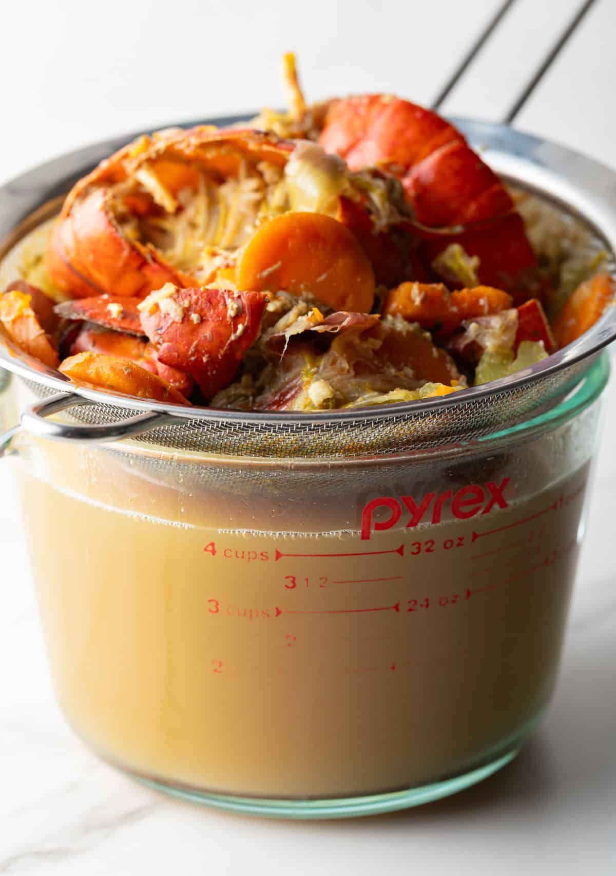 Cooked lobster tails are being strained with a mesh strainer into a glass measuring bowl.