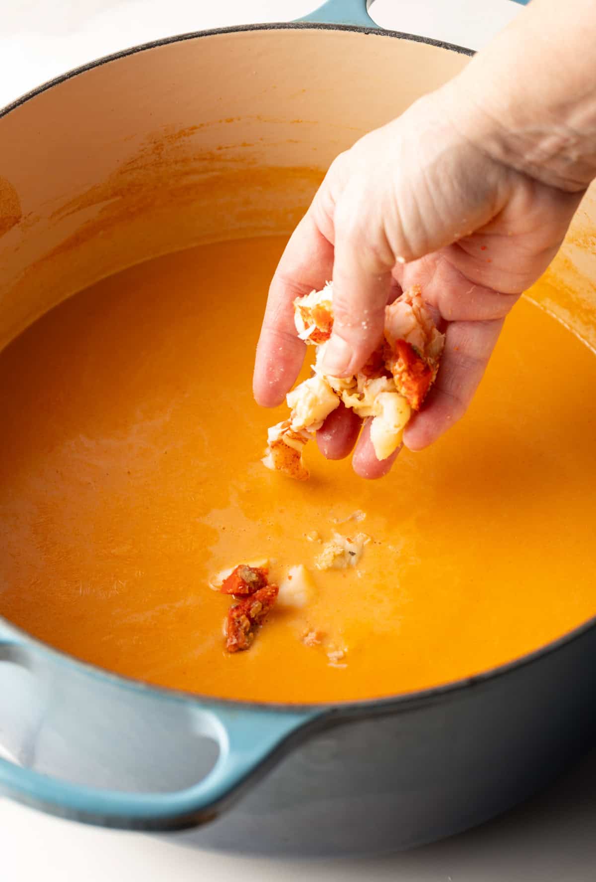 Lobster chunks are being added to a pot full of a creamy lobster bisque recipe.