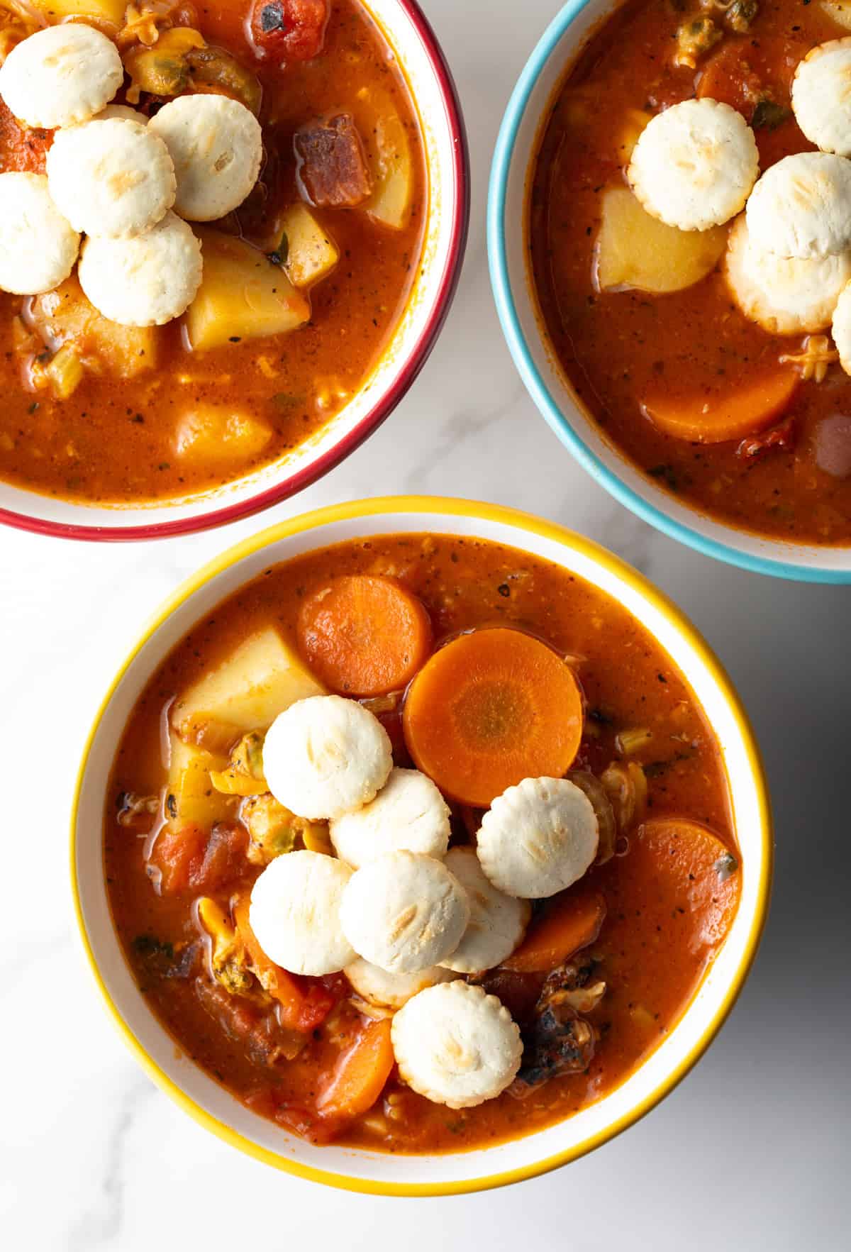 An overhead view of 3 bowls filled with Manhattan-style clam chowder topped with oyster crackers.