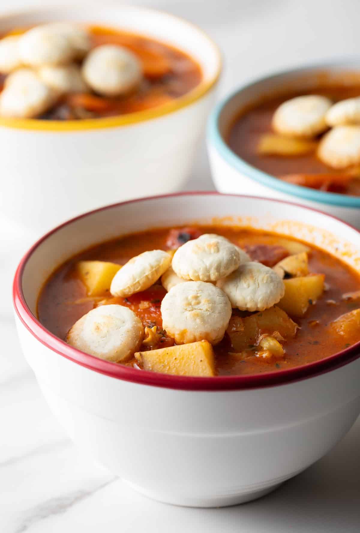 A side view of a bowl filled with Manhattan-style clam chowder topped with oyster crackers.