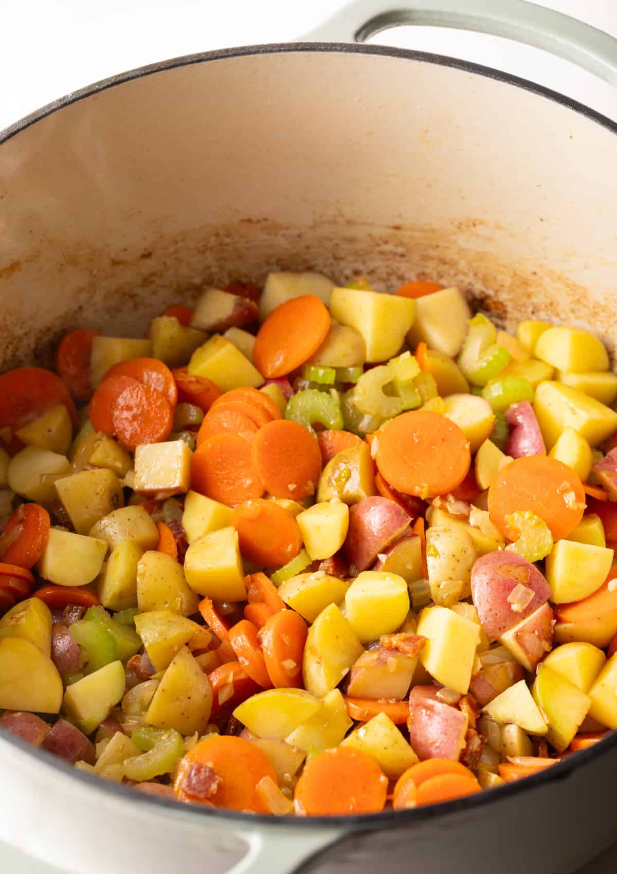 A cooking pot filled with bacon and vegetables, being cooked for a Manhattan clam chowder recipe.