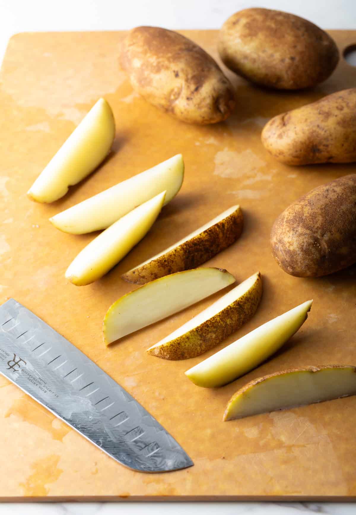 Raw potato wedges sitting on a cutting board next to a knife.
