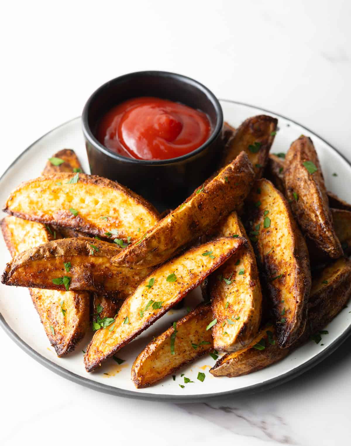 A plate of homemade baked potato wedges with a ramekin of ketchup.
