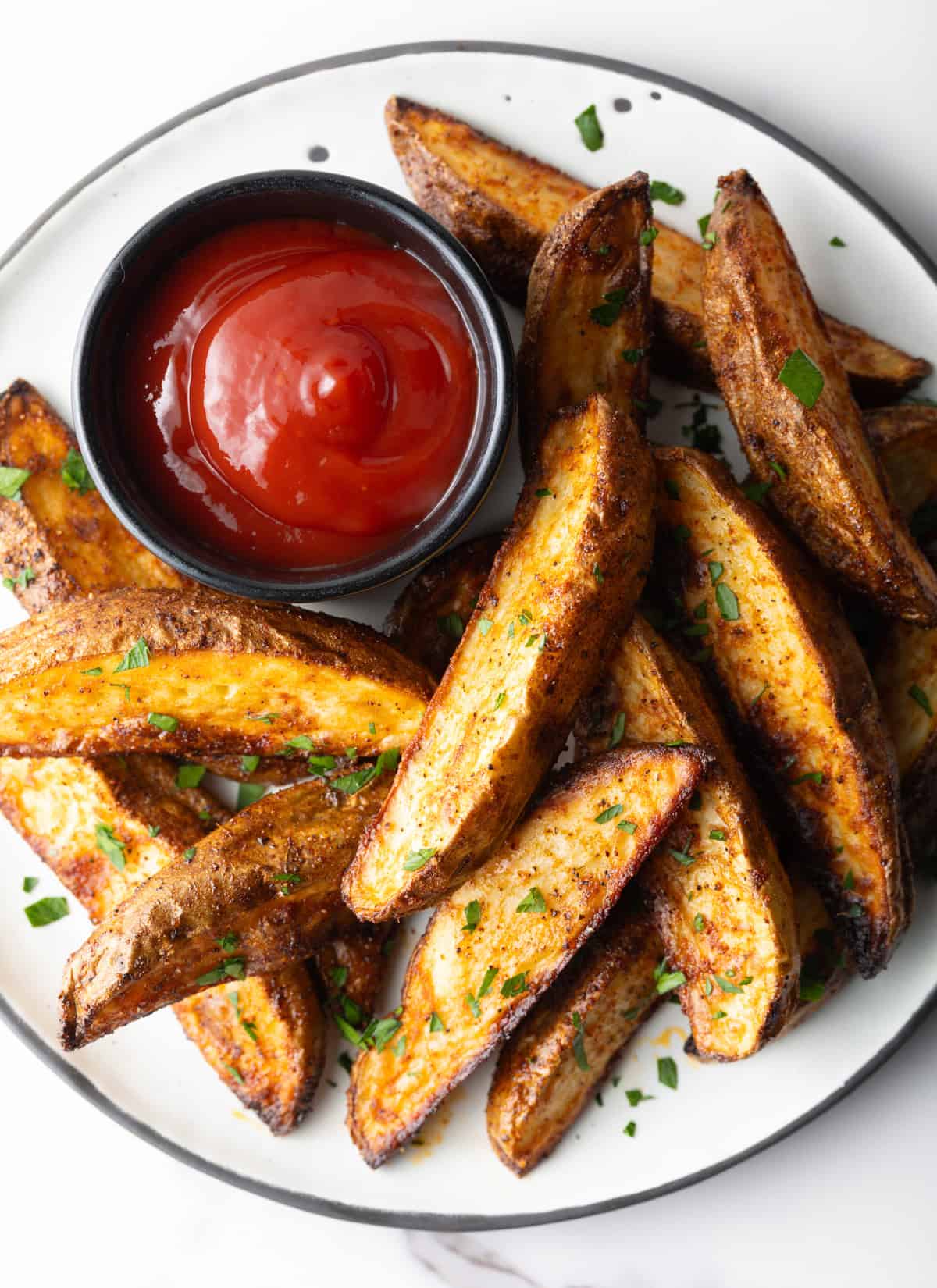 A plate of easy baked potato wedges with a side of ketchup.