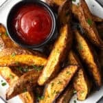 A plate of crispy oven baked potato wedges with a ramekin full of ketchup.