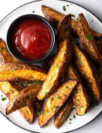 A plate of crispy oven baked potato wedges with a ramekin full of ketchup.