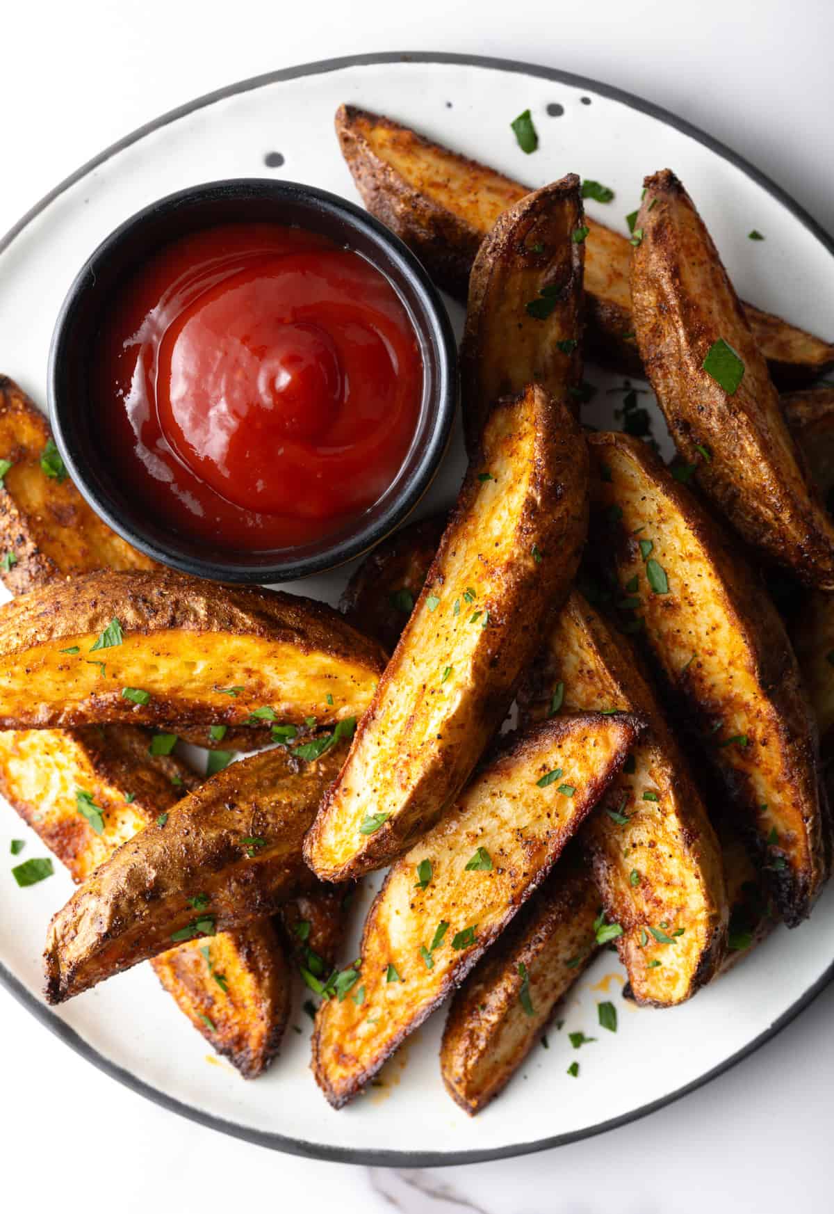 A plate of crispy oven baked potato wedges with a ramekin full of ketchup.