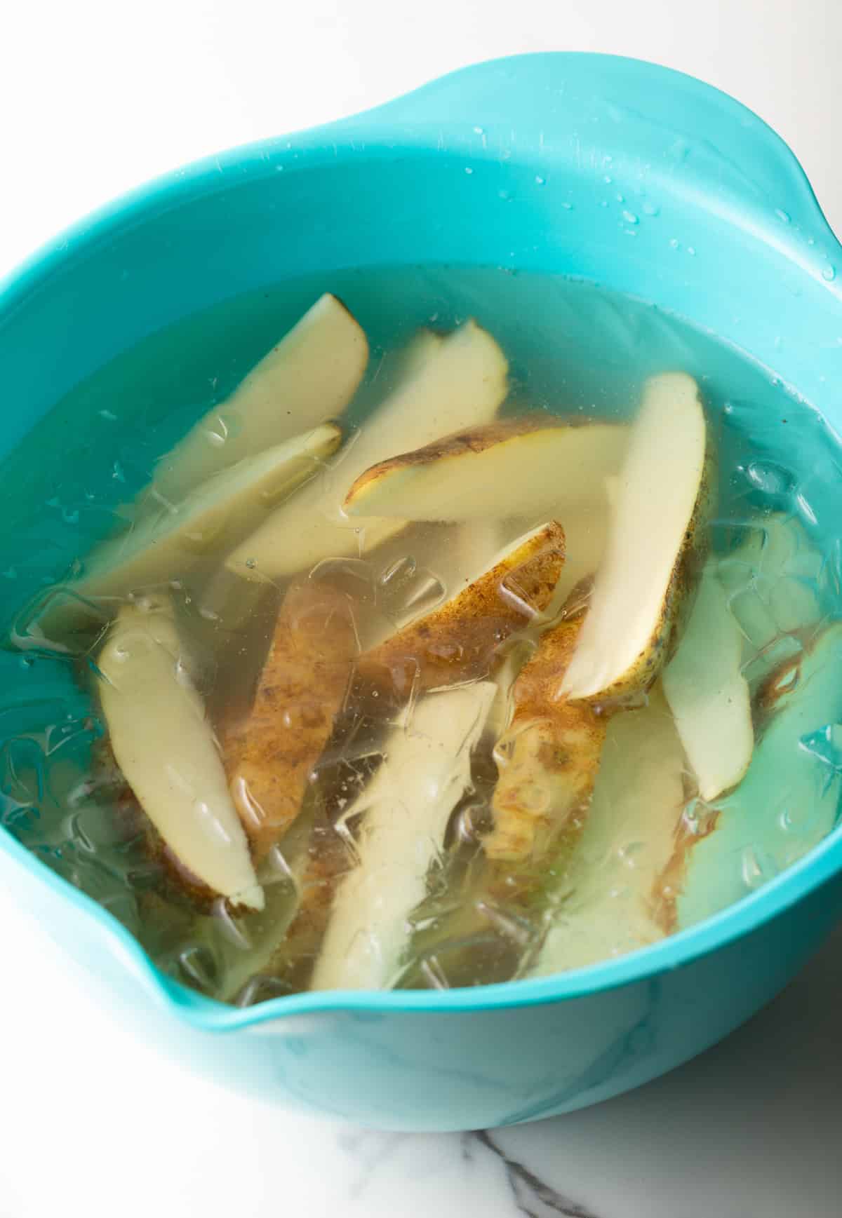 Raw potato wedges sitting in an ice bath in a blue bowl.