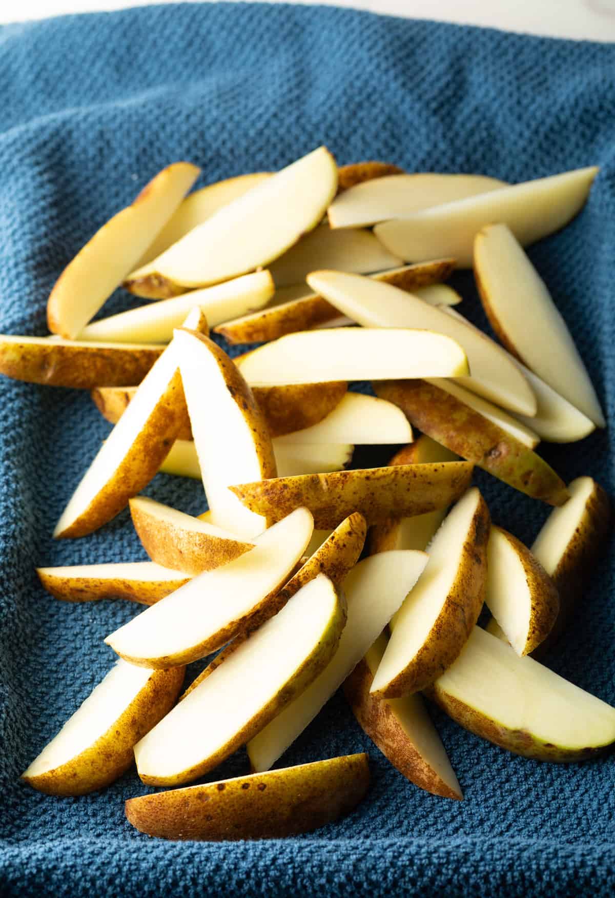 Raw potato wedges are draining on a towel to remove excess moisture.
