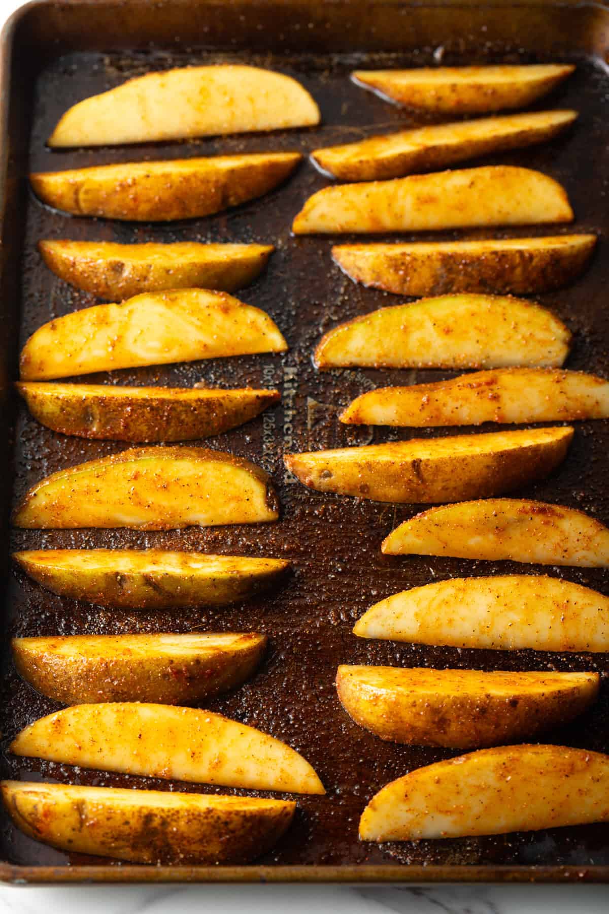 Homemade potato wedges arranged on a baking sheet, ready for baking.