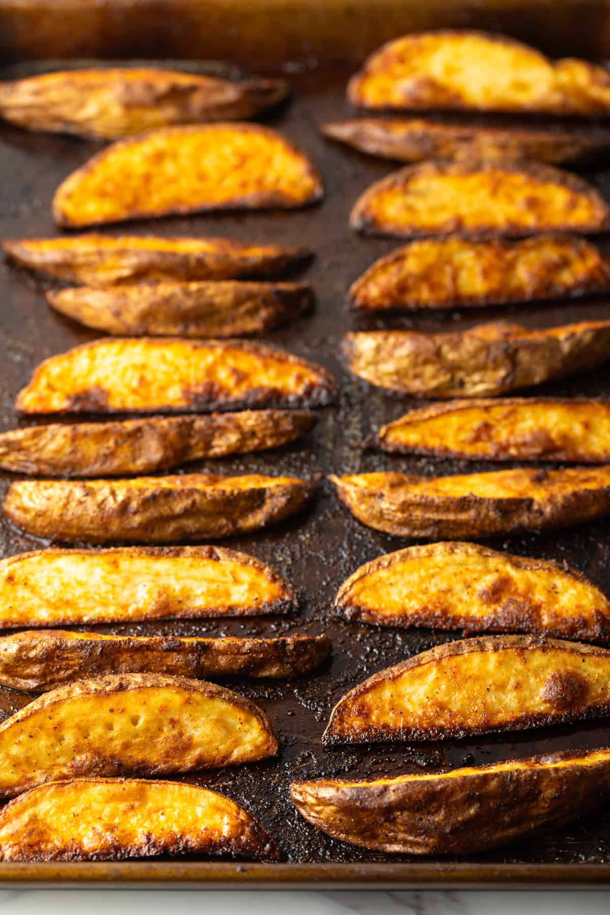 Freshly baked oven baked potato wedges on a black baking sheet.