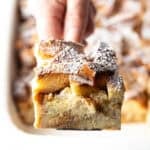 A slice of French toast casserole overnight recipe being held up with a spatula over a white baking dish.