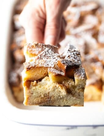 A slice of French toast casserole overnight recipe being held up with a spatula over a white baking dish.
