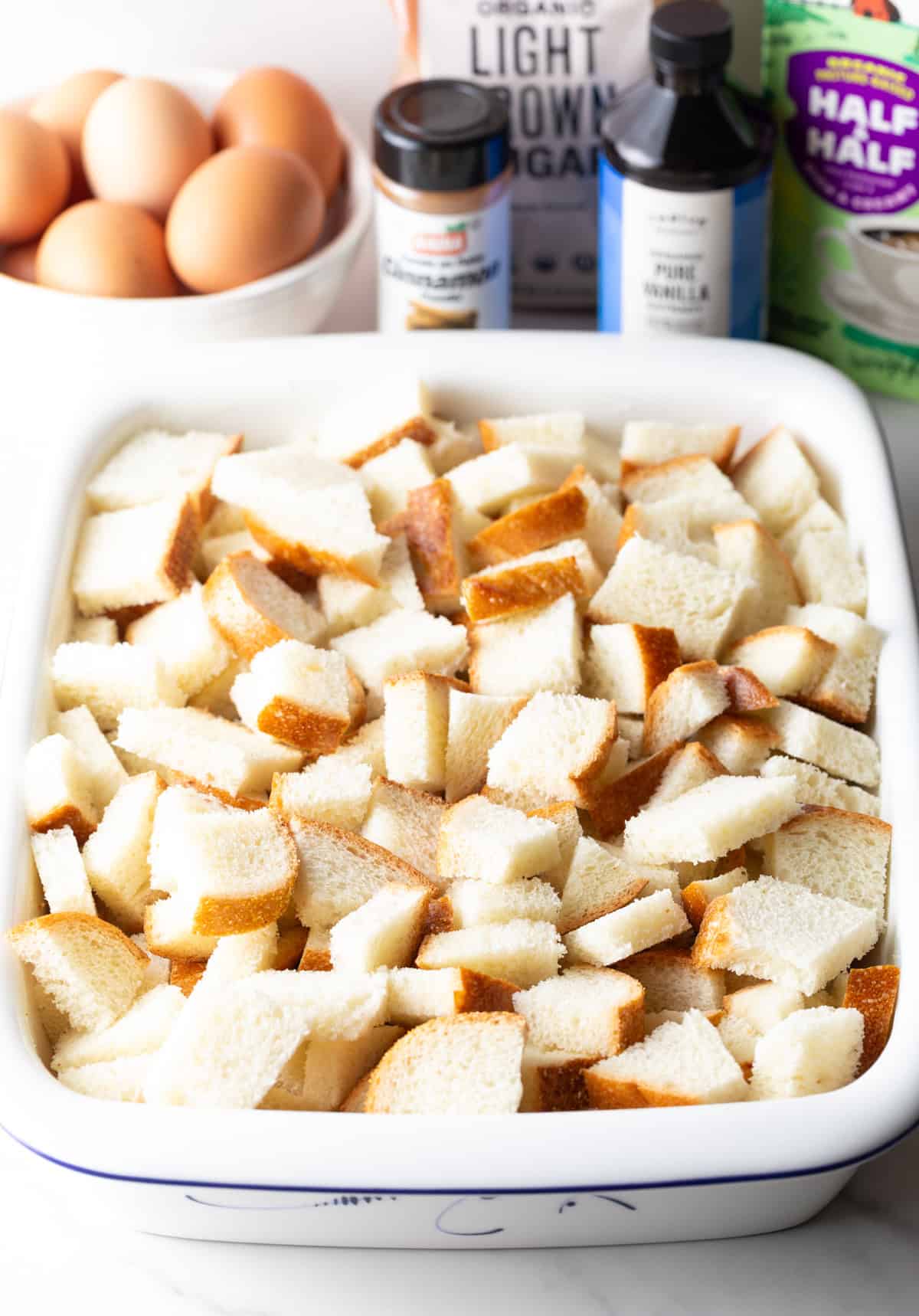 A white baking dish filled with chopped chunks of bread for French toast casserole.
