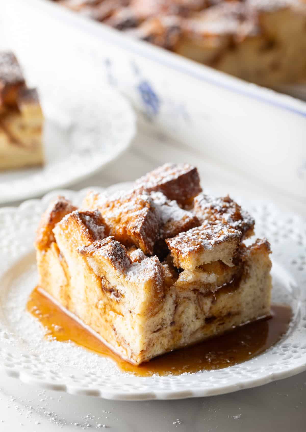 A slice of easy overnight French toast casserole surrounded by syrup, sitting on a white plate.