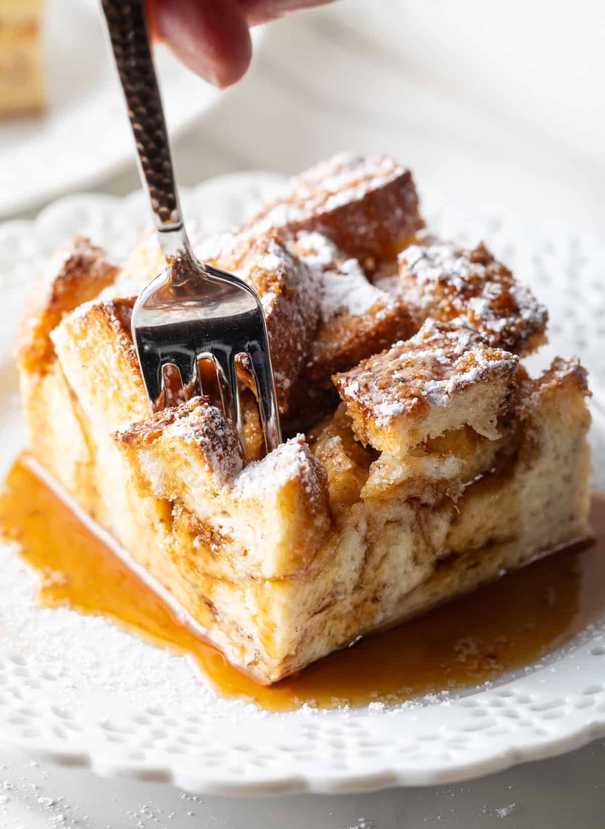 A fork is taking a bite out of a serving of make-ahead French toast casserole.