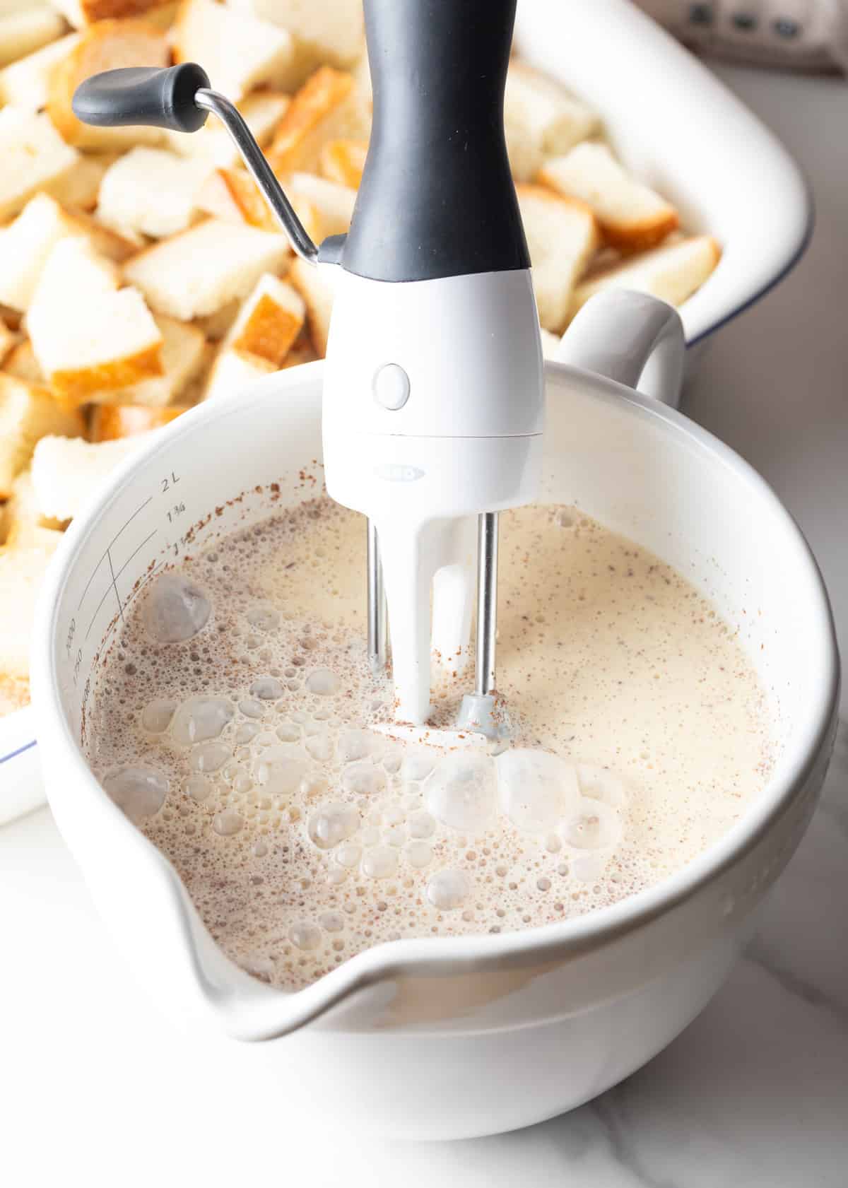 A cream and egg mixture is being beaten with a whisk in a white bowl.