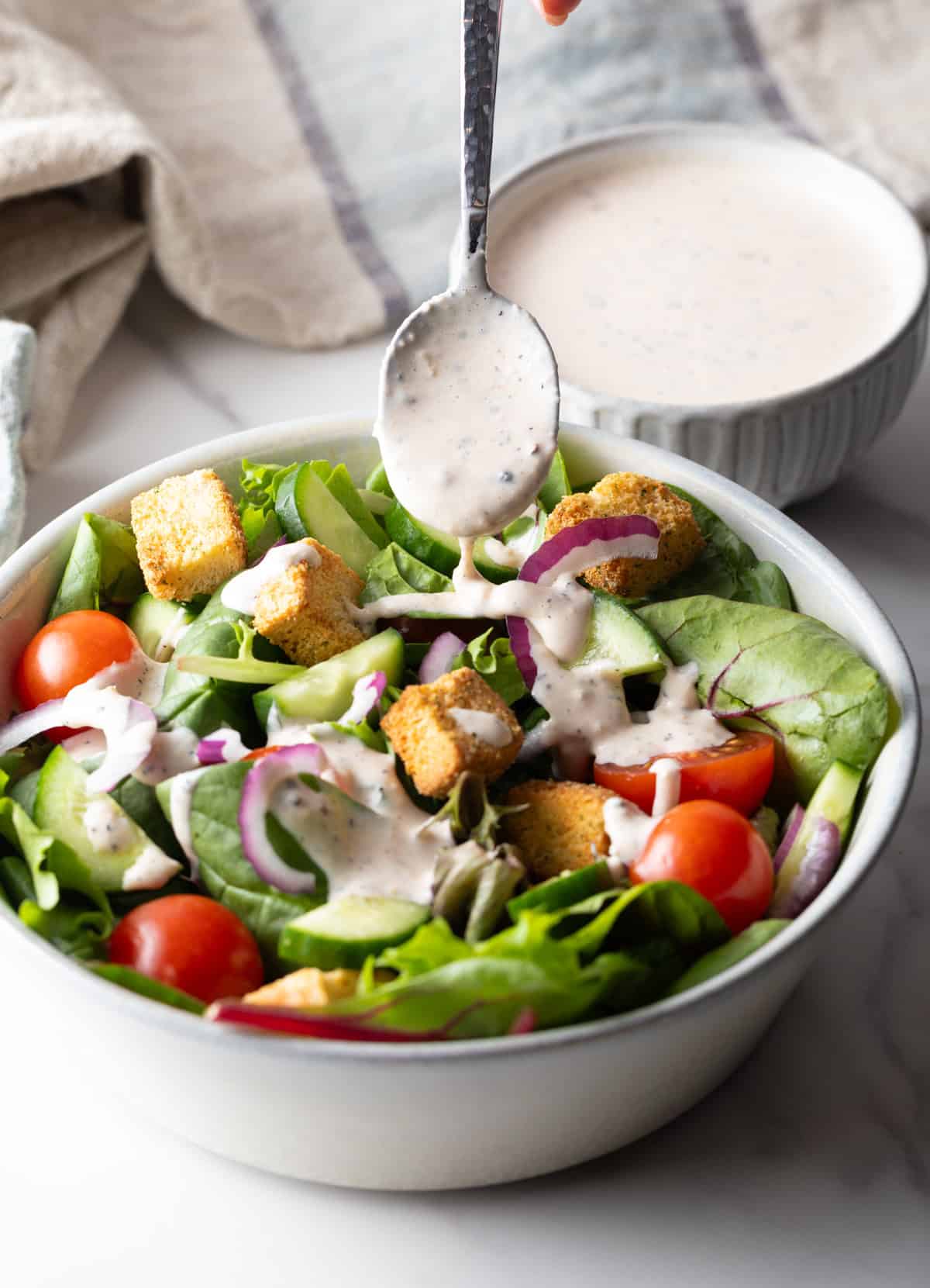 A metal spoon is ladling parmesan peppercorn dressing over a garden salad.